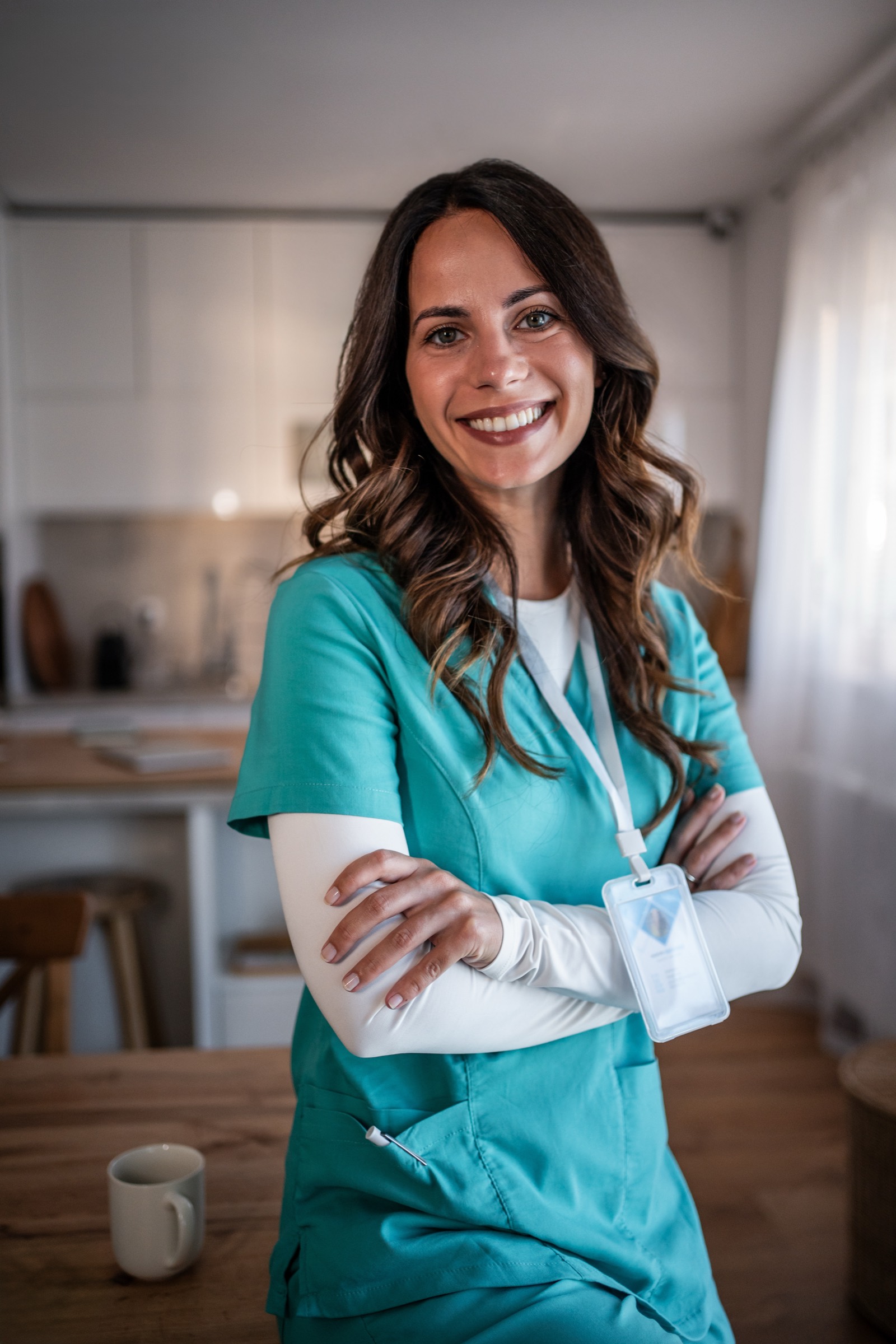 A smiling caregiver in scrubs standing in a home kitchen